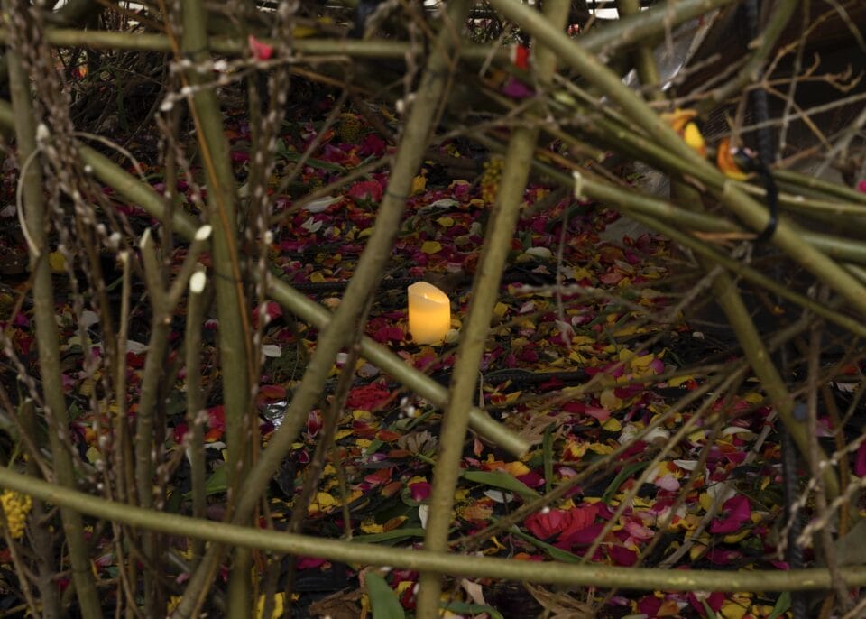 a close up image peering through an orb of flowers and stems to reveal a candle nested in a pool of soil and flowers below