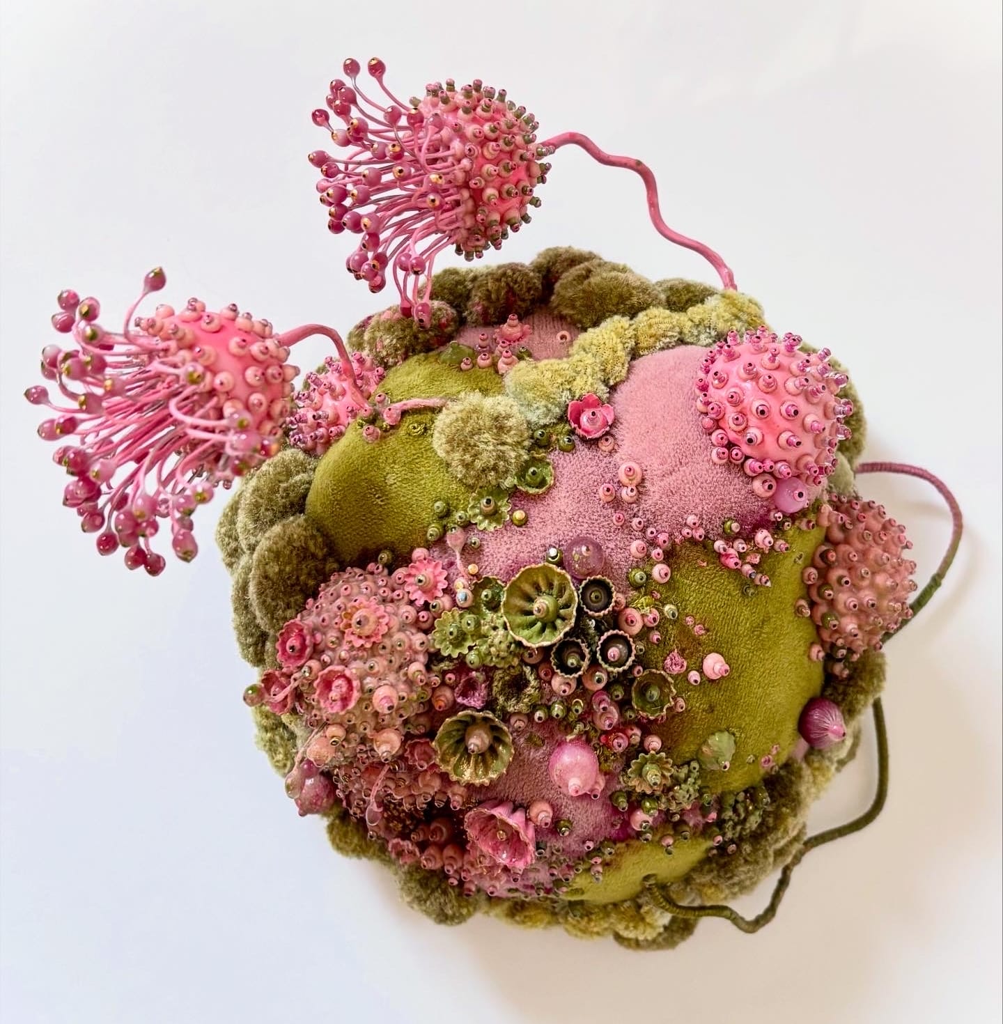 An intricate wall sculpture by Amy Gross of moss and pink flora made from paper and beads
