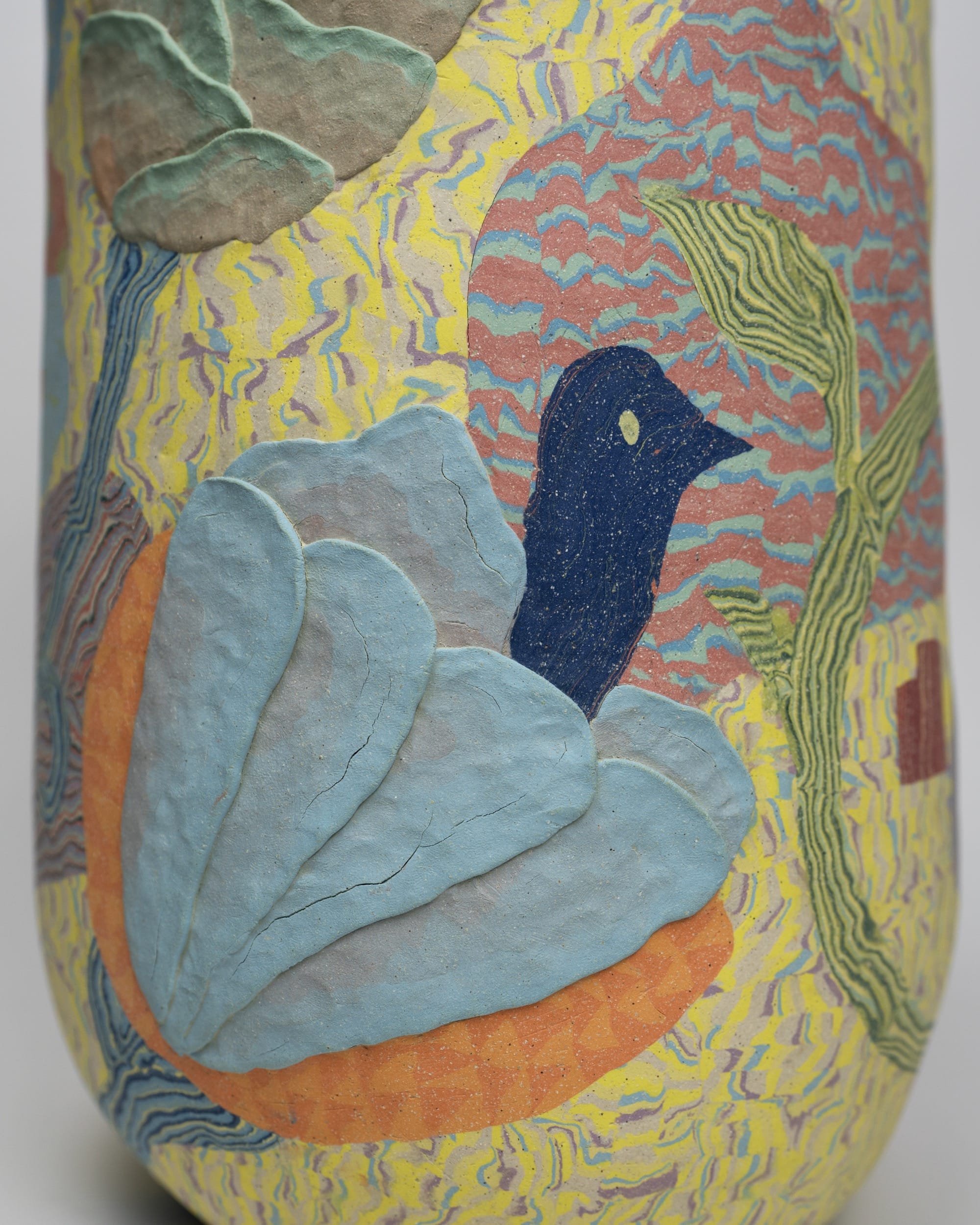 a detail of a ceramic sculpture by Janny Baek with patterned colorful clay and a blue bird form emerging from a lighter blue flower