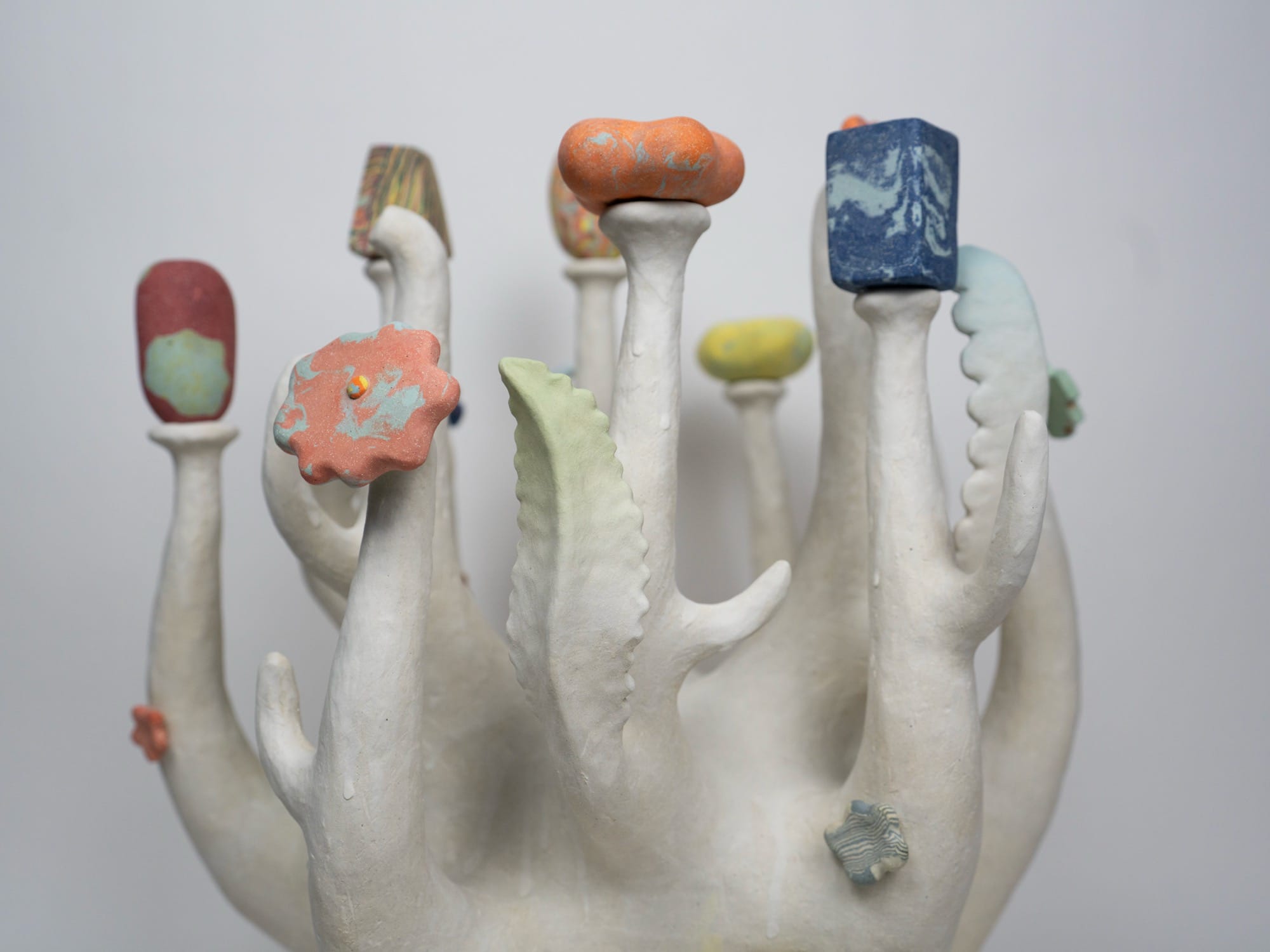a detail of a ceramic sculpture by Janny Baek with colorful organic forms emerging from white shoots