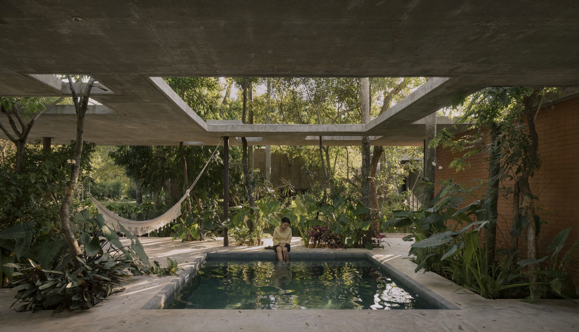 The interior pool of a contemporary concrete, glass, and steel home amid trees and tropical plants