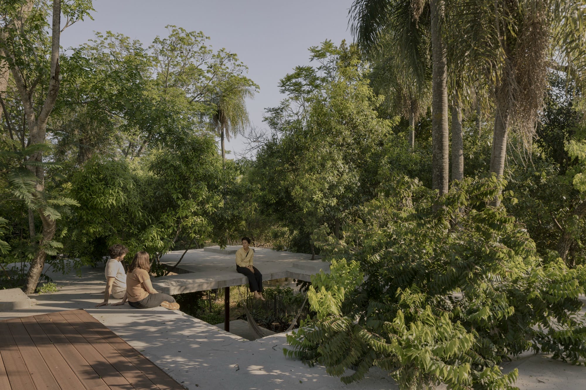 People sit on a concrete canopy of a contemporary home amid tropical trees and plants