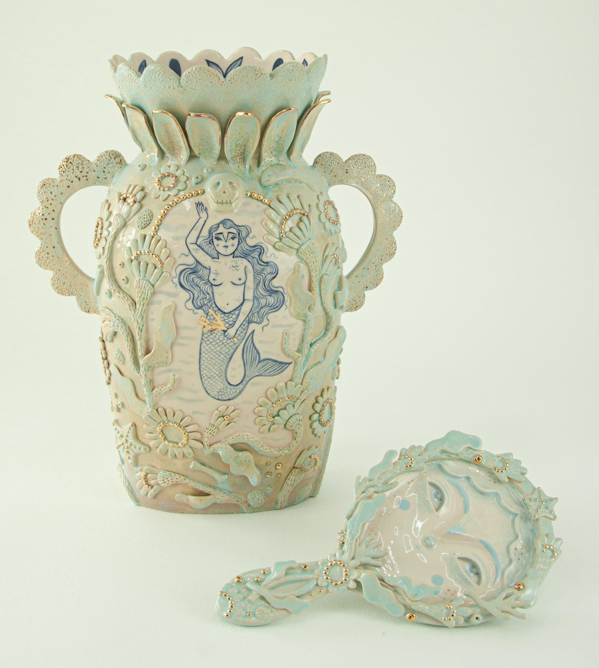 a ceramic sculpture by Abi Castillo of an intricately ornate vase and handheld mirror, adorned with mermaid details and gold accents